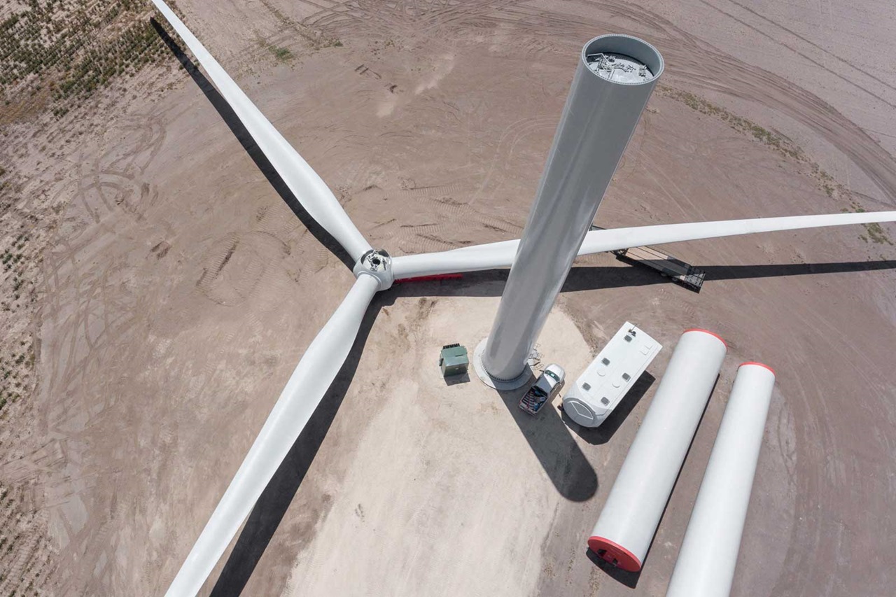Aerial view of a wind turbine with three blades, a tall tower, and nearby components on a dry landscape.