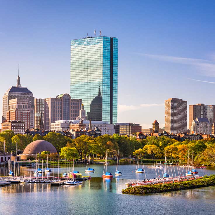 A panoramic view of Boston's skyline featuring the Prudential Tower amidst green parks and sailboats on the water.