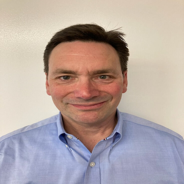A man wearing a light blue shirt in front of a plain white background.