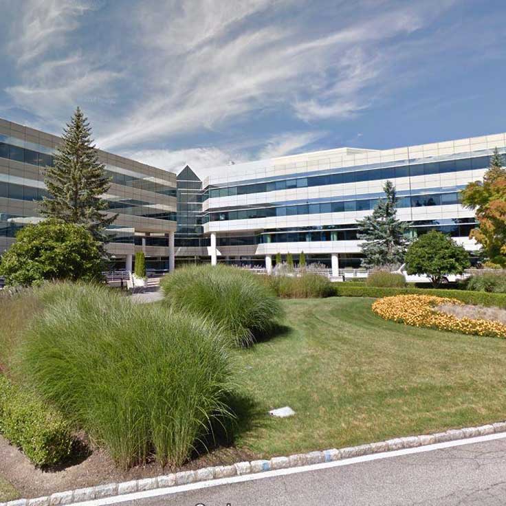 A modern office building with glass facades surrounded by landscaped greenery and colourful flower beds under a blue sky.