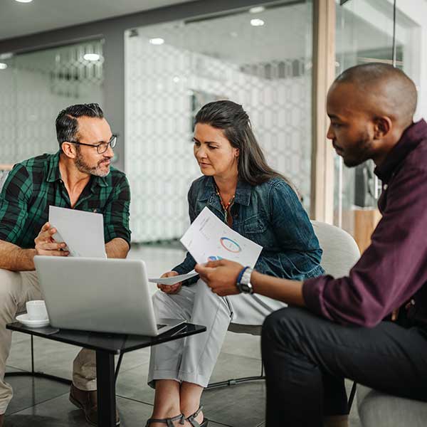 A group of three people engaged in a discussion around a laptop, sharing documents in a modern office setting.