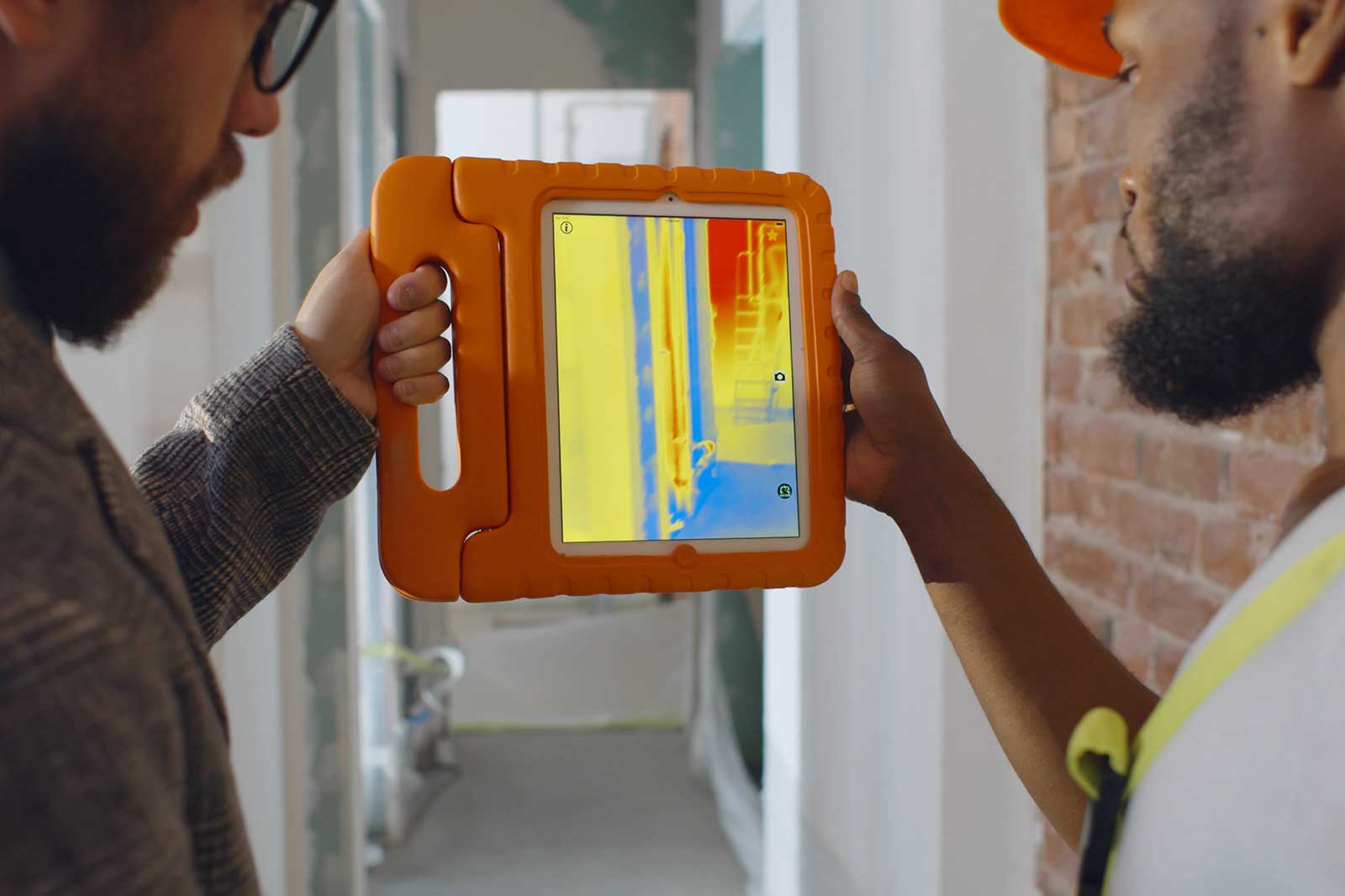 Two individuals are examining a thermal imaging tablet displaying a vibrant heat map in a construction environment.