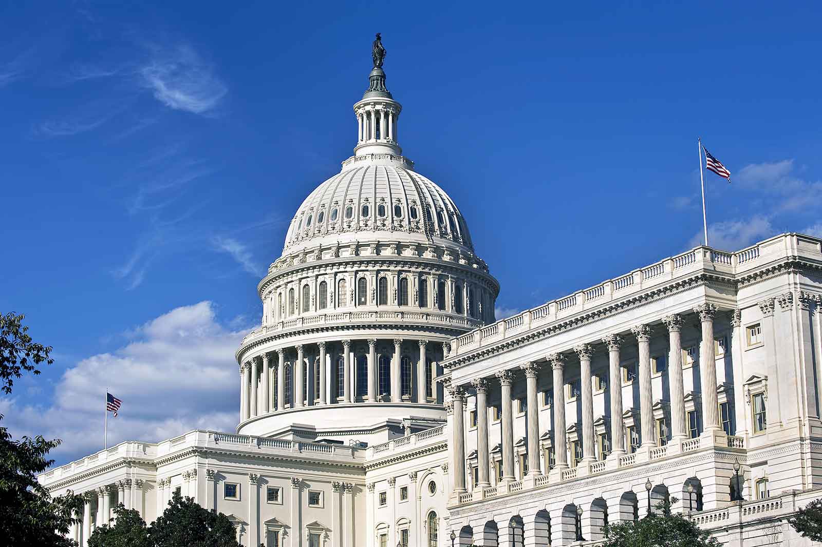 The United States Capitol building stands majestically under a bright blue sky, showcasing its iconic dome and grand columns.