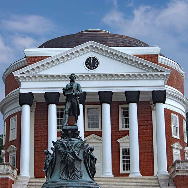 A grand building with white columns and a dome, featuring a clock, and a statue in front depicting a historical figure.
