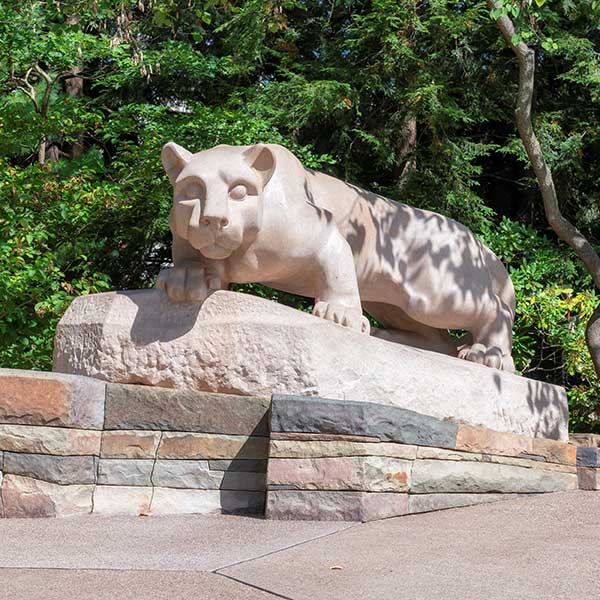 A stone statue of a panther crouching on a rock, surrounded by greenery and trees.