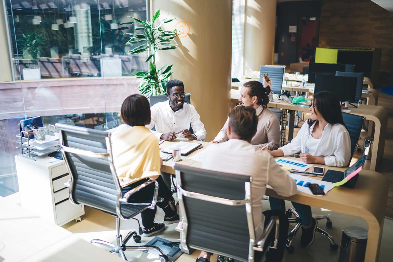 A group of professionals engaged in a meeting at a modern office, surrounded by plants and office equipment.