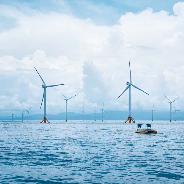A serene seascape featuring multiple wind turbines in the distance and a small boat floating on calm waters under a cloudy sky.