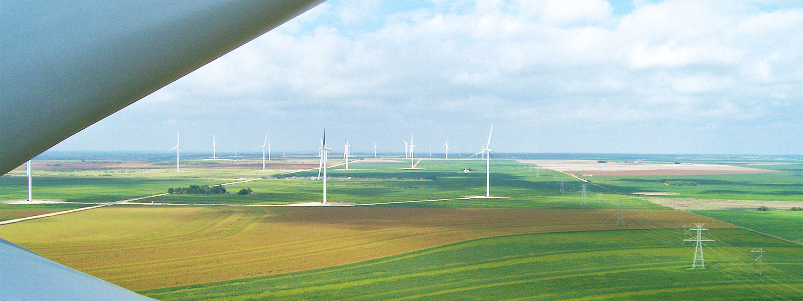 A vast landscape featuring wind turbines, green fields, and a blue sky with clouds.