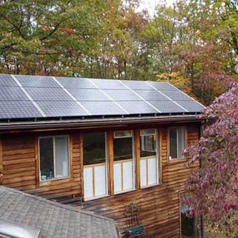 A solar panel installation on a wooden house roof, surrounded by autumn trees with colourful leaves.