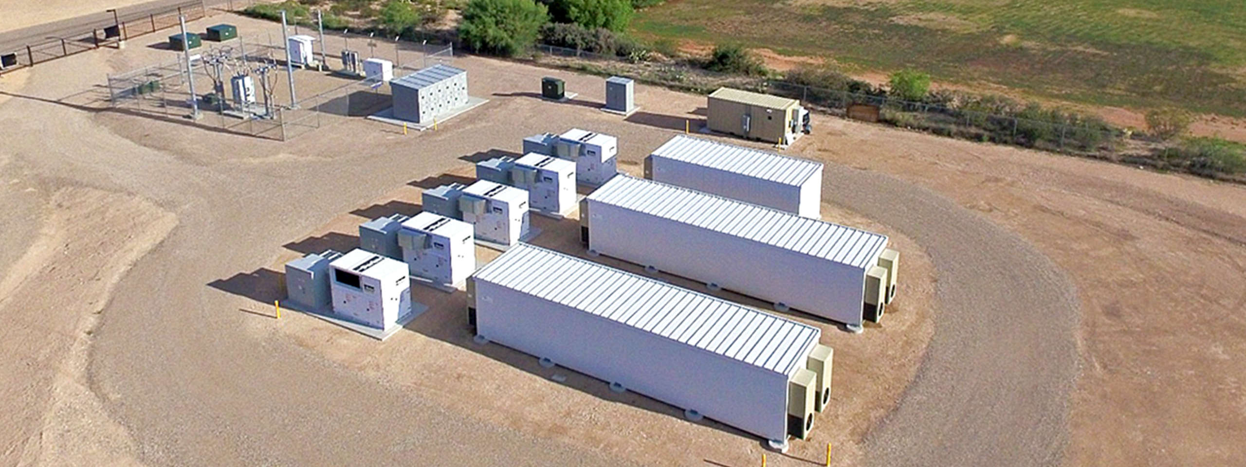 An overhead view of several containers on a vast sandy area, featuring some electrical installations in the background.
