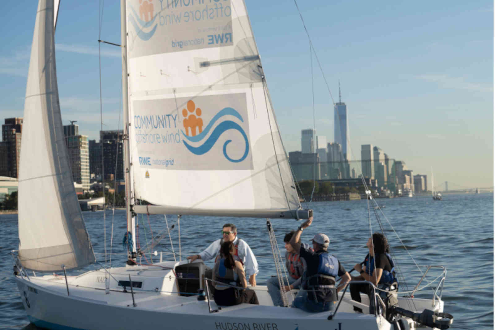 A group of people sailing on the Hudson River, with city skyline visible in the background under a clear blue sky.