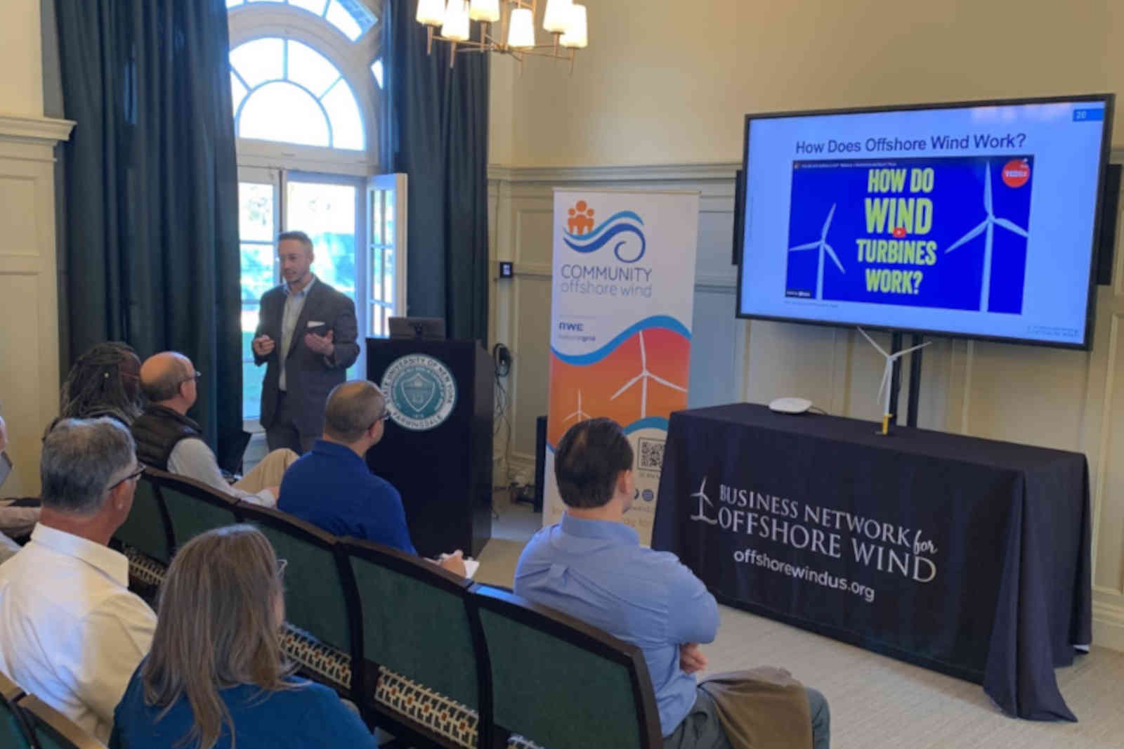A presenter discusses offshore wind energy with an audience, featuring a screen displaying 'How does offshore wind work?