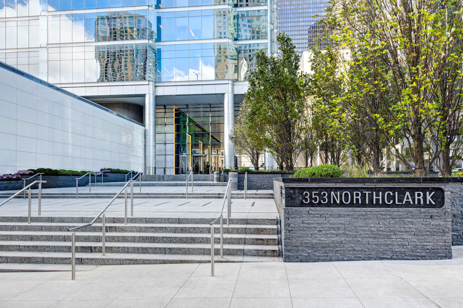 The entrance of 353 North Clark features modern architecture, stone steps, greenery, and reflective glass panels.