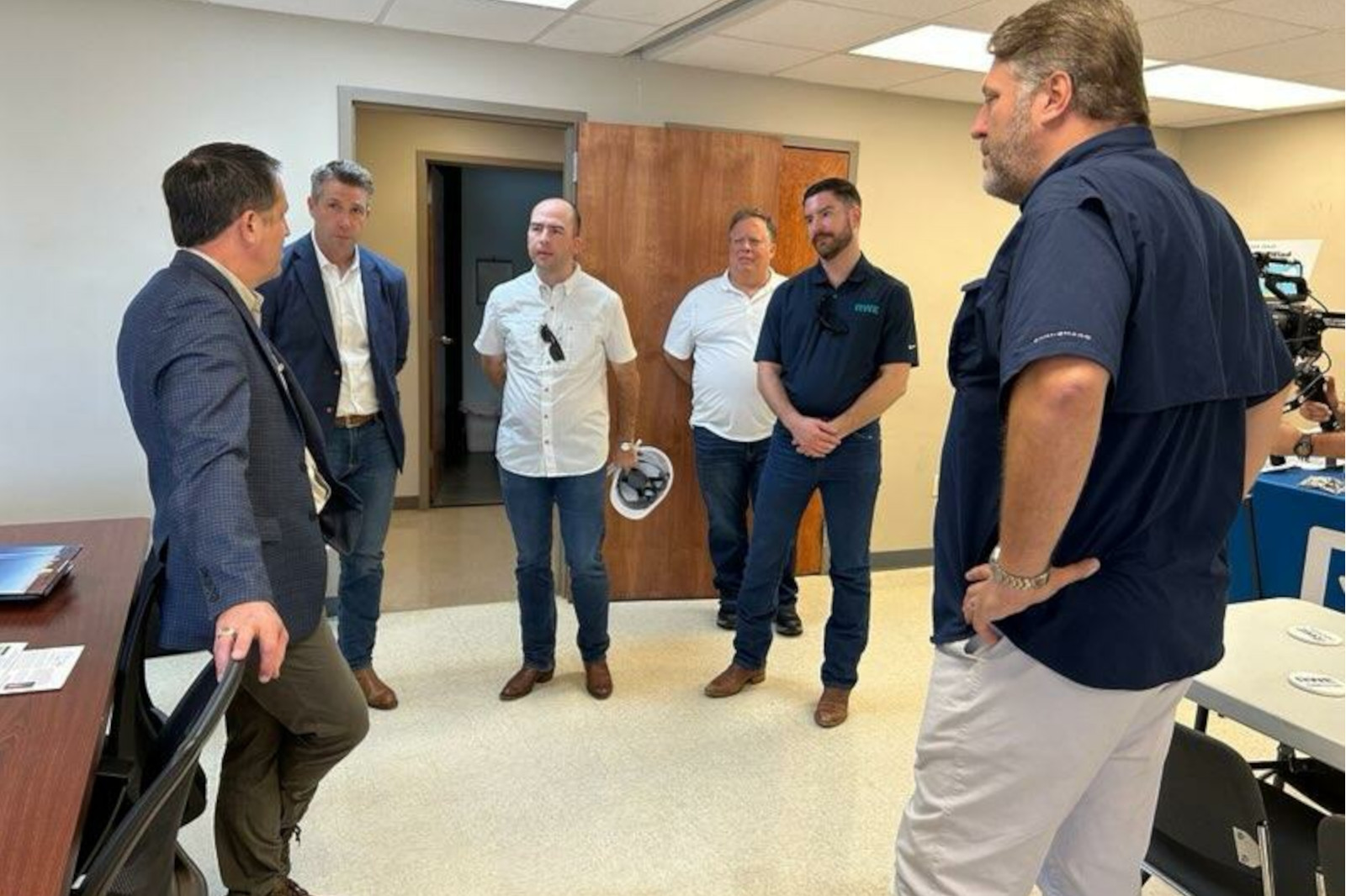 A group of men in a meeting room engaging in conversation. They are dressed in business casual attire and appear focused.