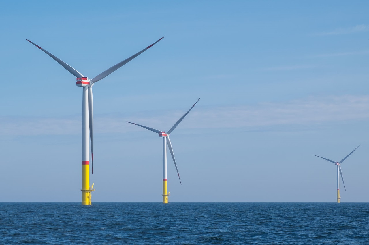 Three offshore wind turbines stand in the ocean under a clear sky, showcasing renewable energy technology.