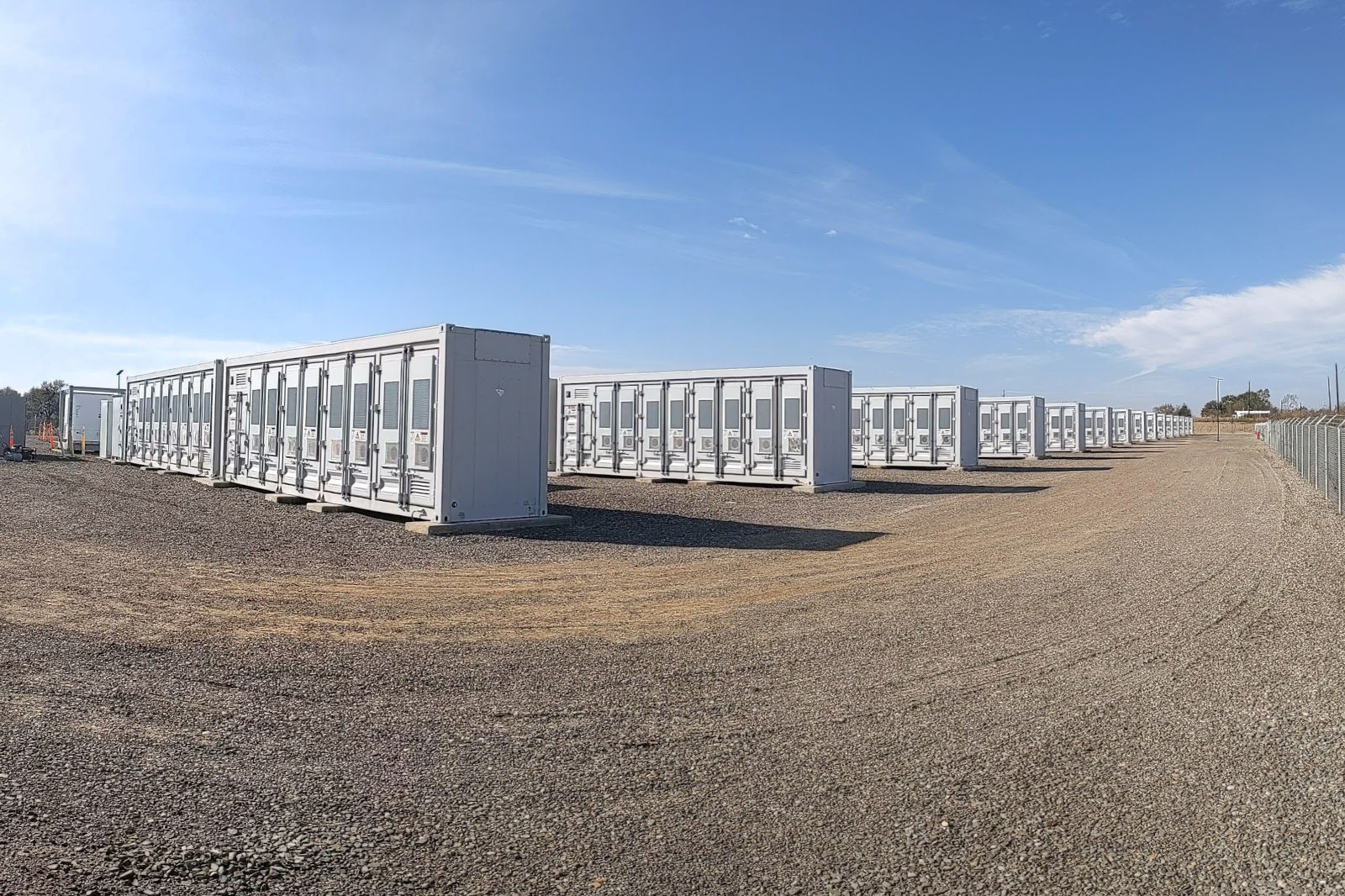 A series of white shipping containers arranged in rows on a gravel surface under a clear blue sky.