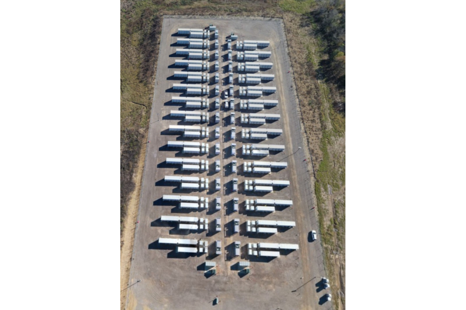 An aerial view of a rectangular parking lot filled with neatly arranged trucks and containers, surrounded by greenery.