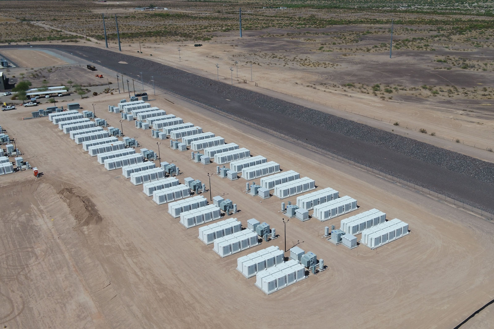 Aerial view of a large solar energy storage facility with numerous white storage containers and electrical equipment in a desert landscape.