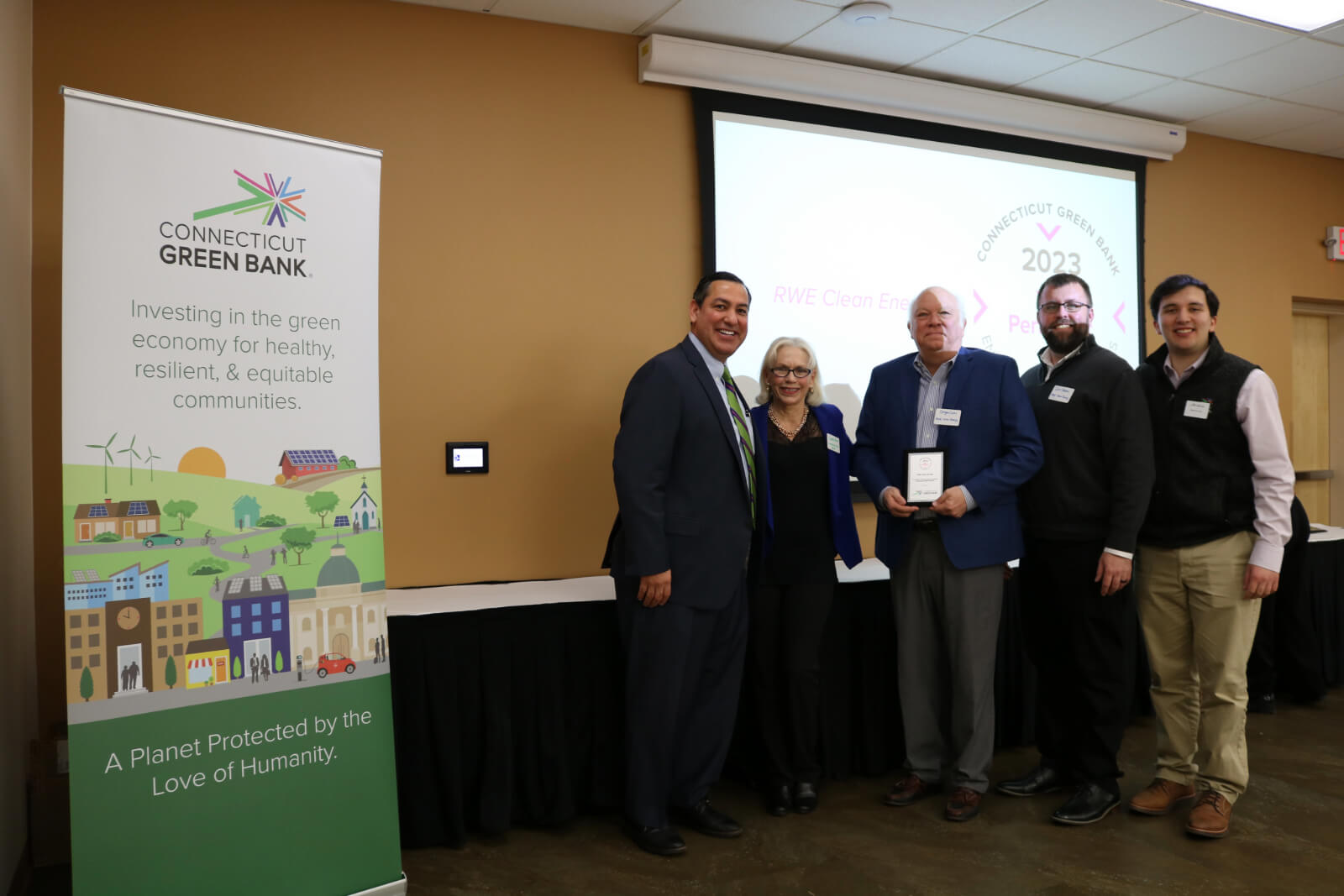 A group of professionals at an event, posing with an award beside a banner for Connecticut Green Bank.