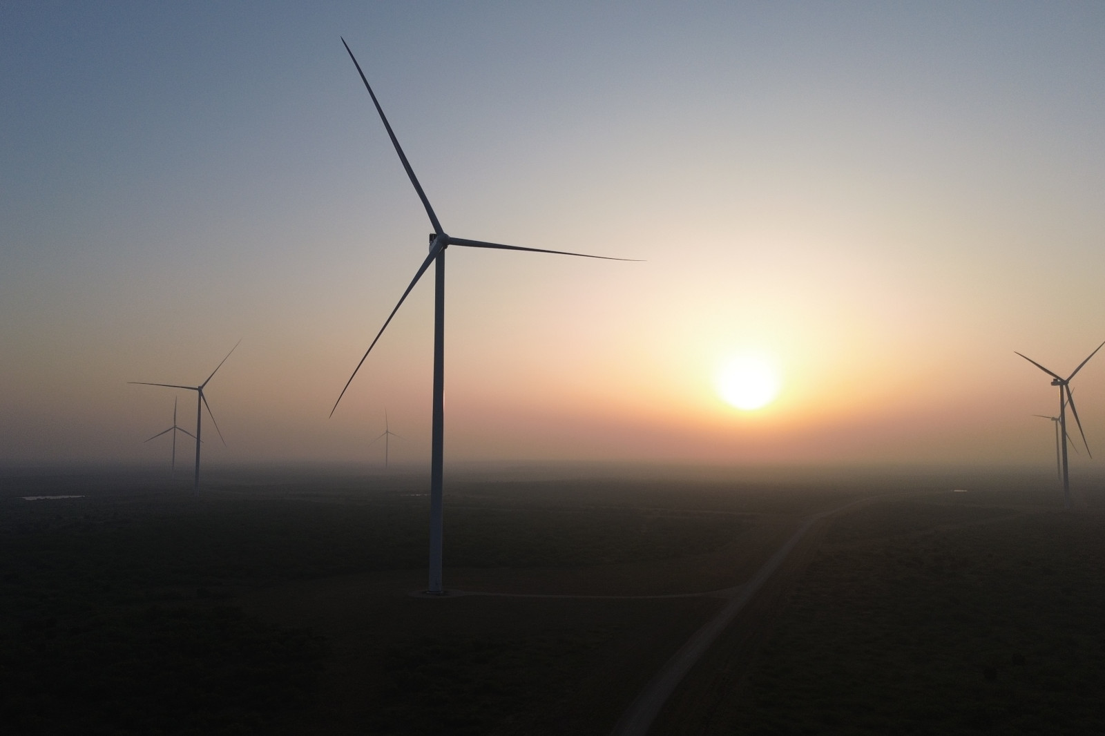 Wind turbines stand silhouetted against a sunset in a misty landscape, showcasing renewable energy.