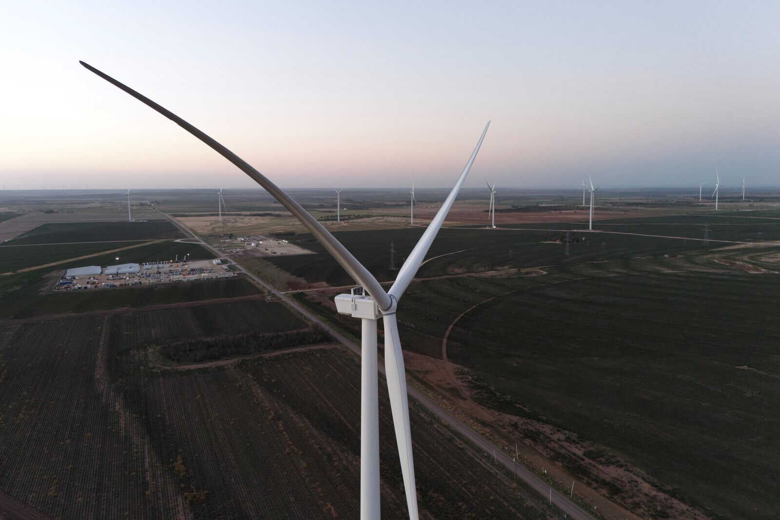 Aerial view of a wind farm with large turbines and a facility in the landscape at dusk.