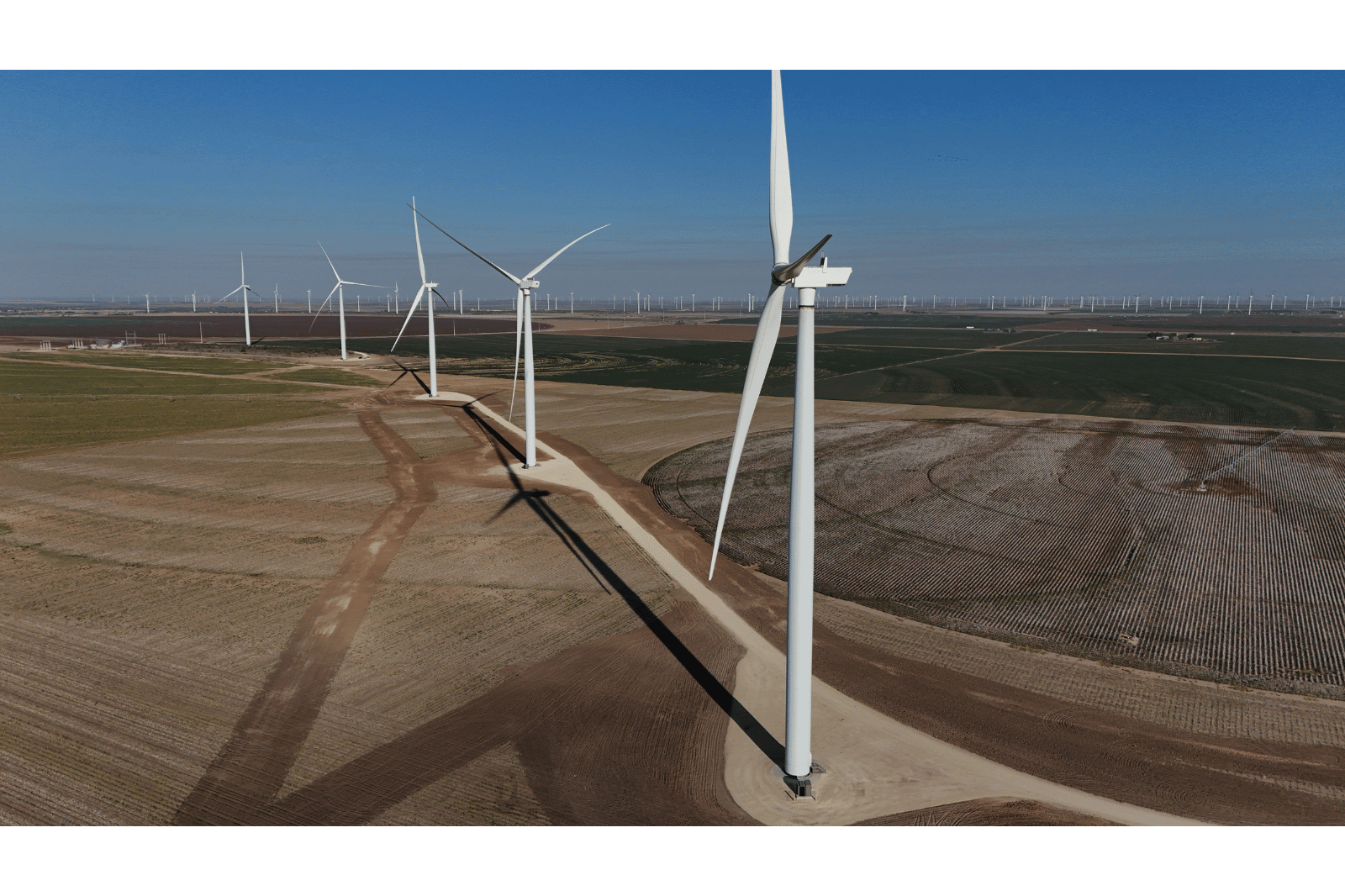 Aerial view of multiple wind turbines on farmland with a clear blue sky in the background.