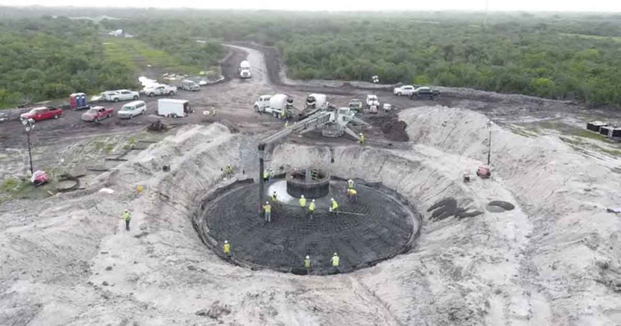 An aerial view of a construction site with workers pouring concrete into a circular foundation surrounded by vehicles and machinery.