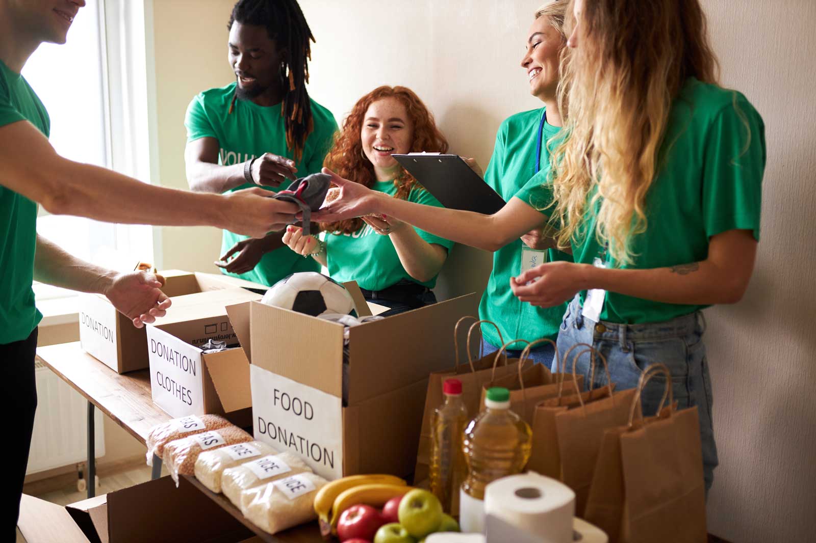 A group of volunteers in green shirts organising donations, including clothes and food, at a table with boxes and bags.
