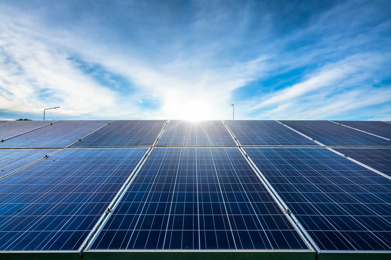 A close-up view of solar panels under a bright sky with the sun shining in the background.