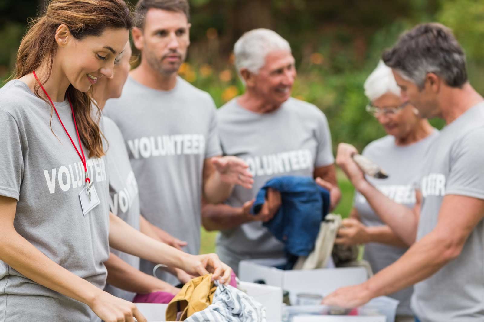 A group of volunteers in grey shirts sorting clothes at an outdoor event, engaging in conversation and collaboration.