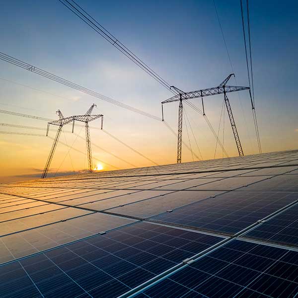 Solar panels in the foreground with power lines and an orange sunset in the background.