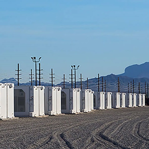 A row of white shipping containers along a gravel path, with power poles and mountains in the background under a clear blue sky.