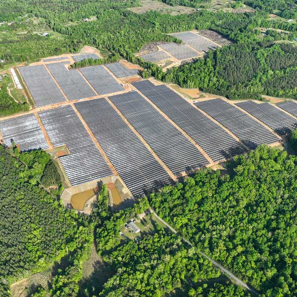 Aerial view of a solar farm with numerous photovoltaic panels set amidst green forest areas.