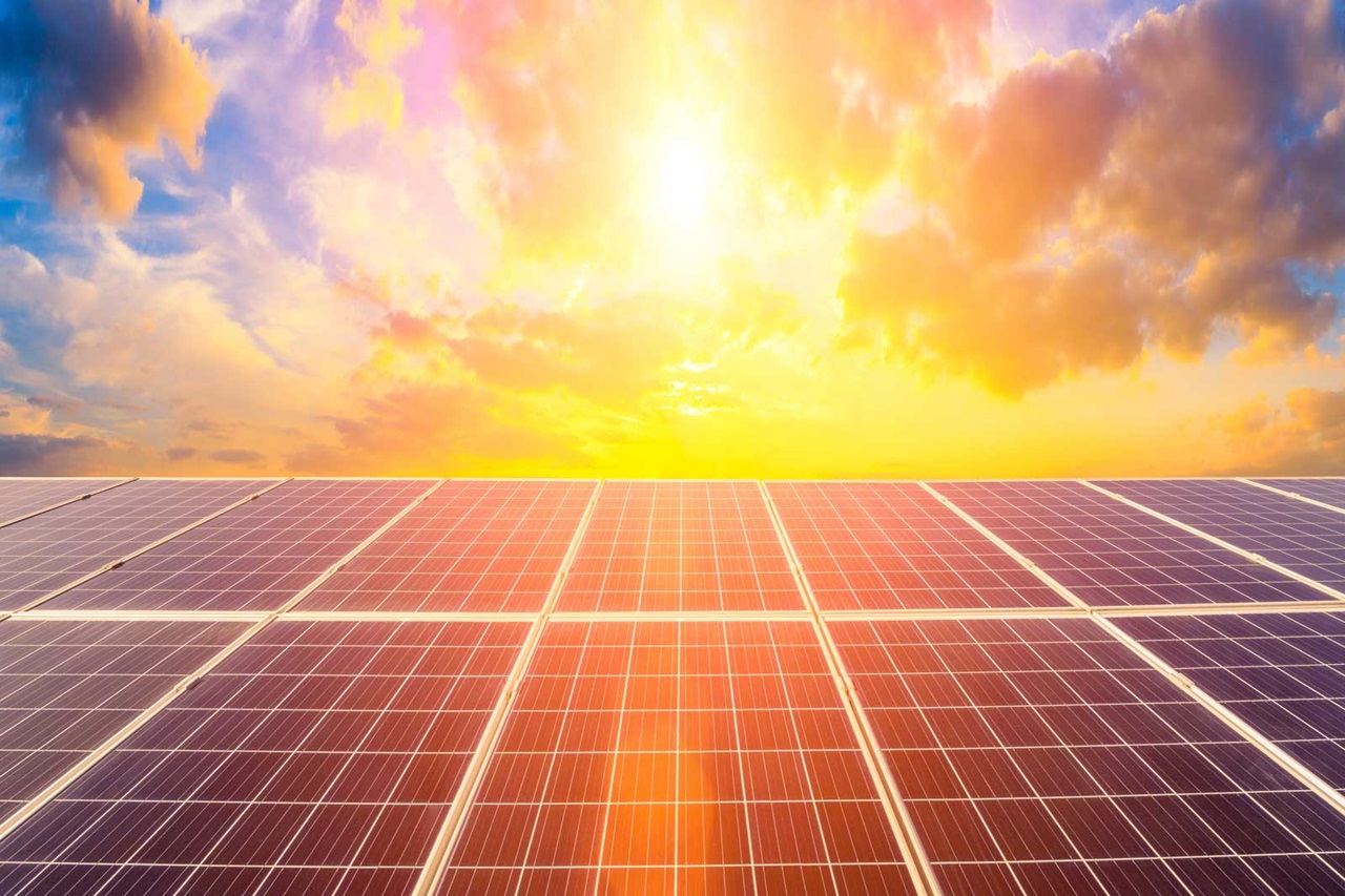 A solar panel field under a vibrant sunrise with colourful clouds and a bright sun illuminating the scene.