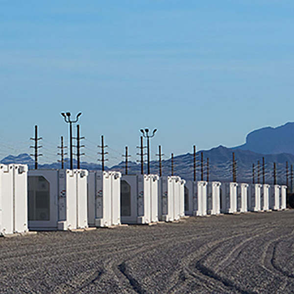 A row of white storage containers on a gravel site, with power lines and mountains in the background under a clear blue sky.
