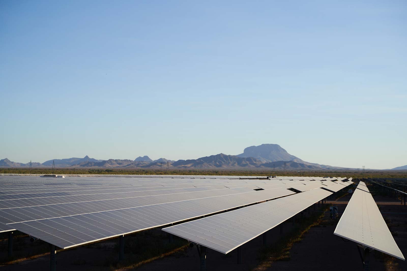 A solar panel farm set against a clear sky and distant mountain range in a desert landscape.