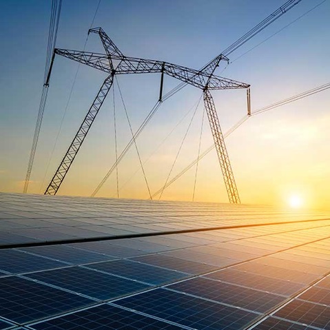 Solar panels reflect sunlight with power lines silhouetted against a vibrant sunrise.