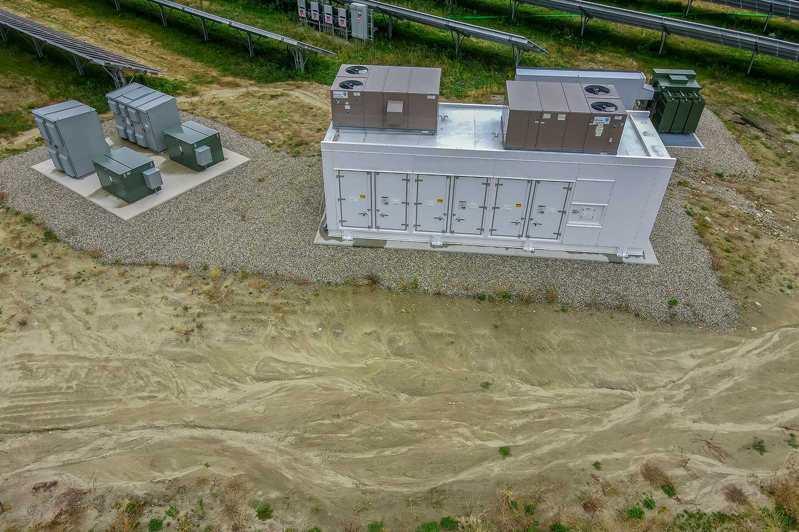 An aerial view of a rectangular facility with several electrical cabinets surrounded by sand and sparse vegetation.
