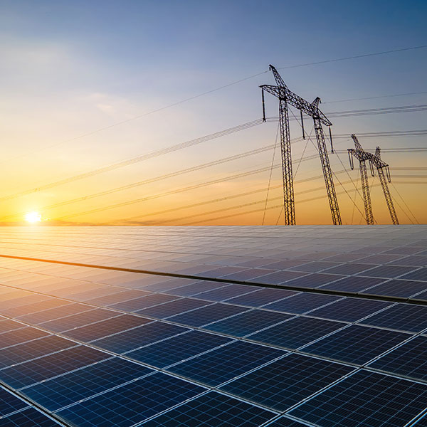 Solar panels reflect the sunset, with high-voltage power lines in the background, illustrating renewable energy.
