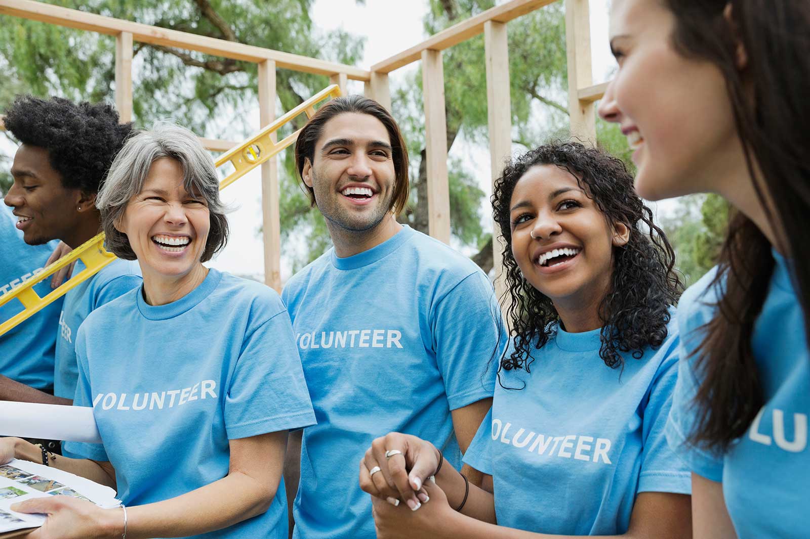 A group of volunteers in blue shirts are engaged in a building project, showcasing teamwork and community spirit outdoors.