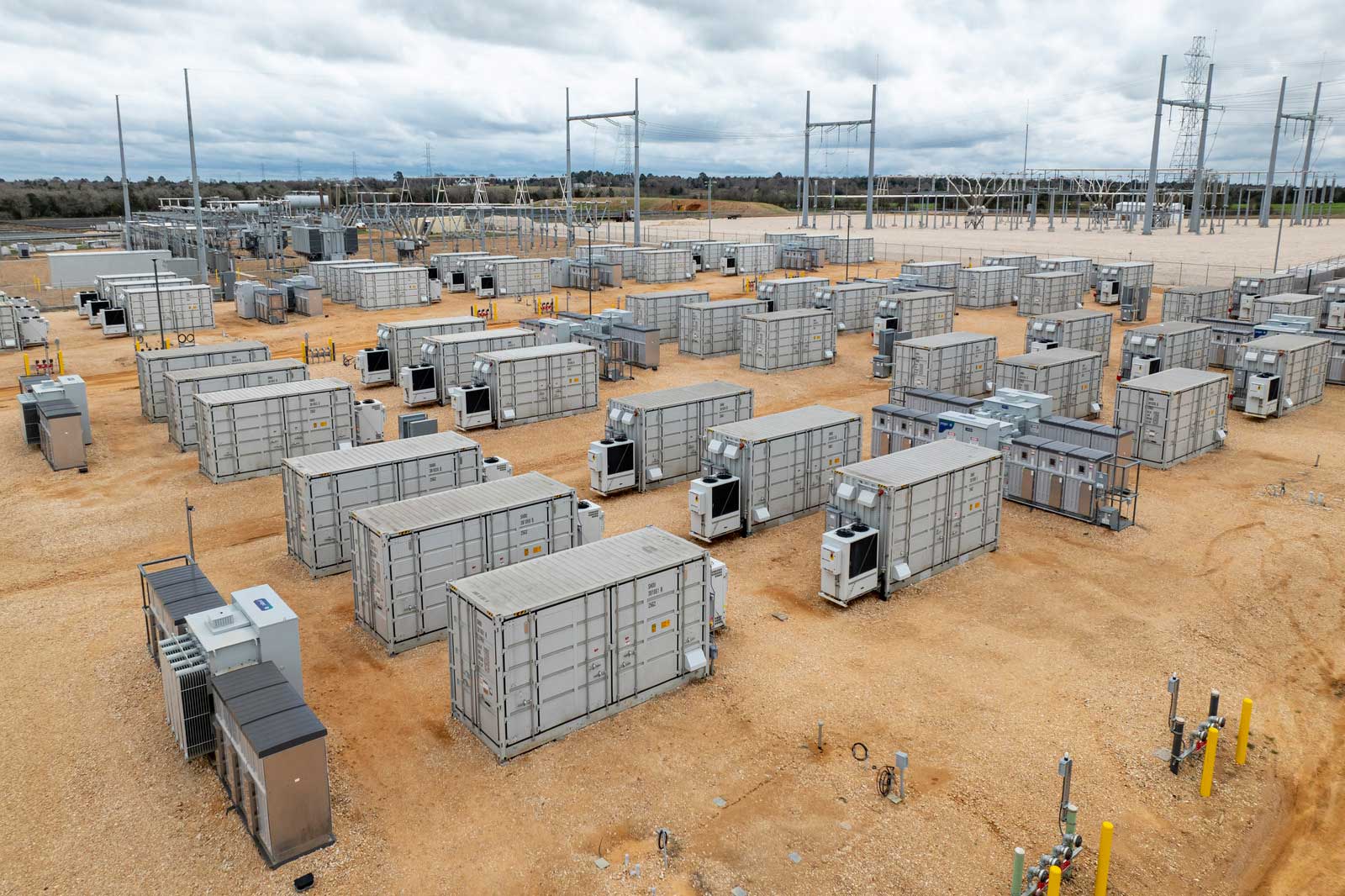 Aerial view of a large energy storage facility featuring numerous grey containers, power poles, and a rugged landscape.
