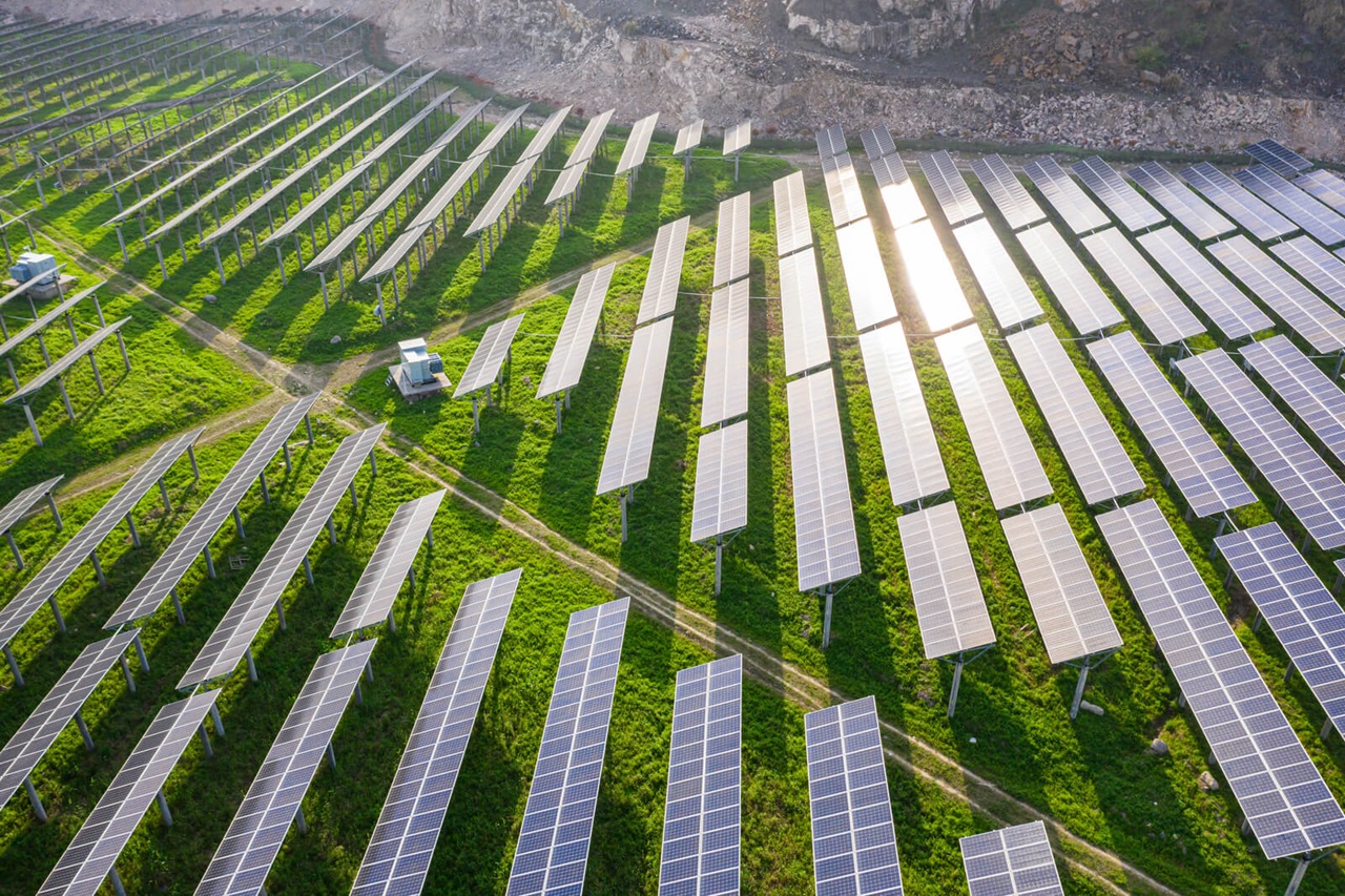 Aerial view of a solar farm with rows of solar panels on green grass under sunlight.
