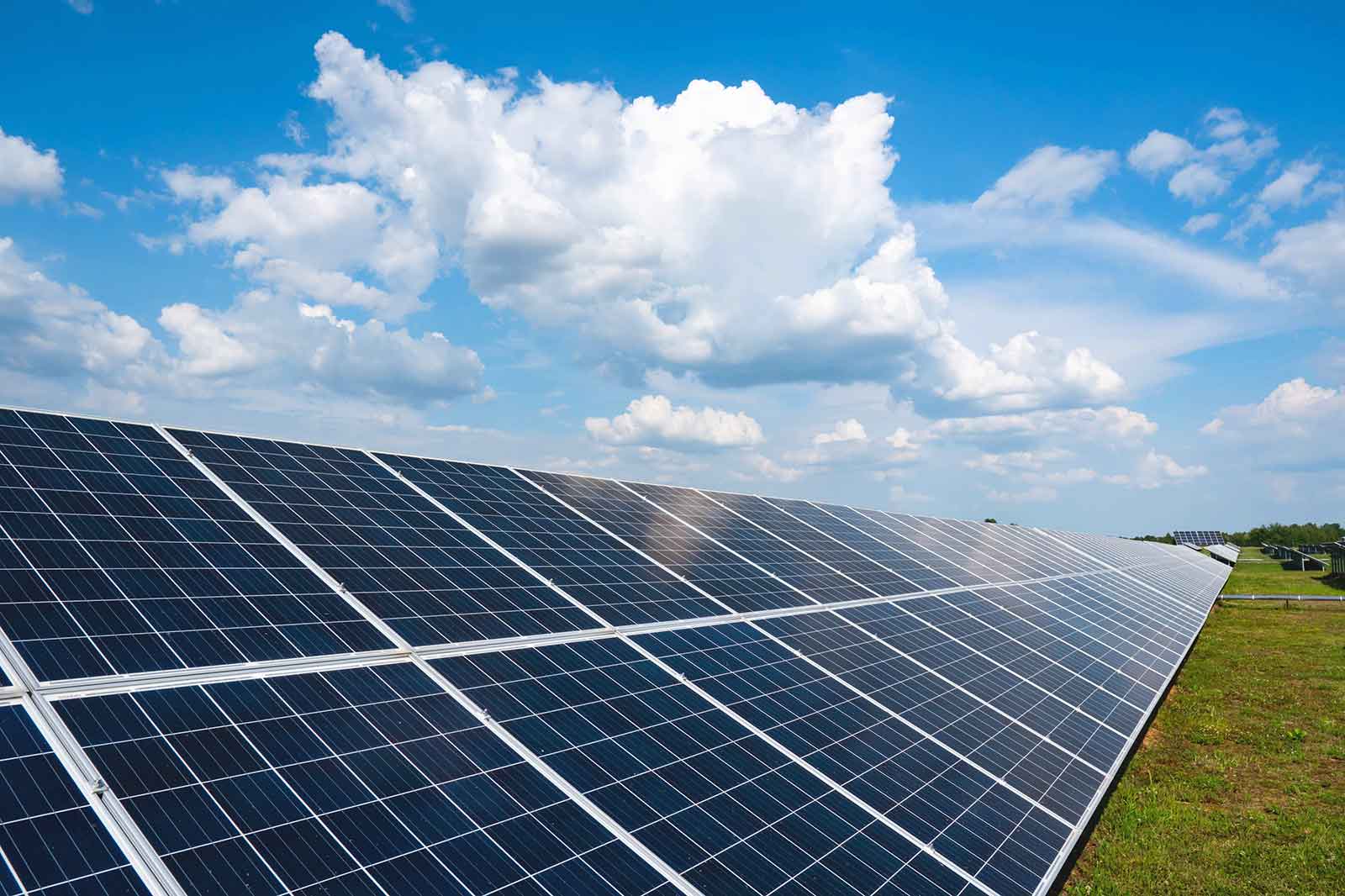 A solar panel farm with rows of photovoltaic panels under a blue sky with fluffy white clouds.