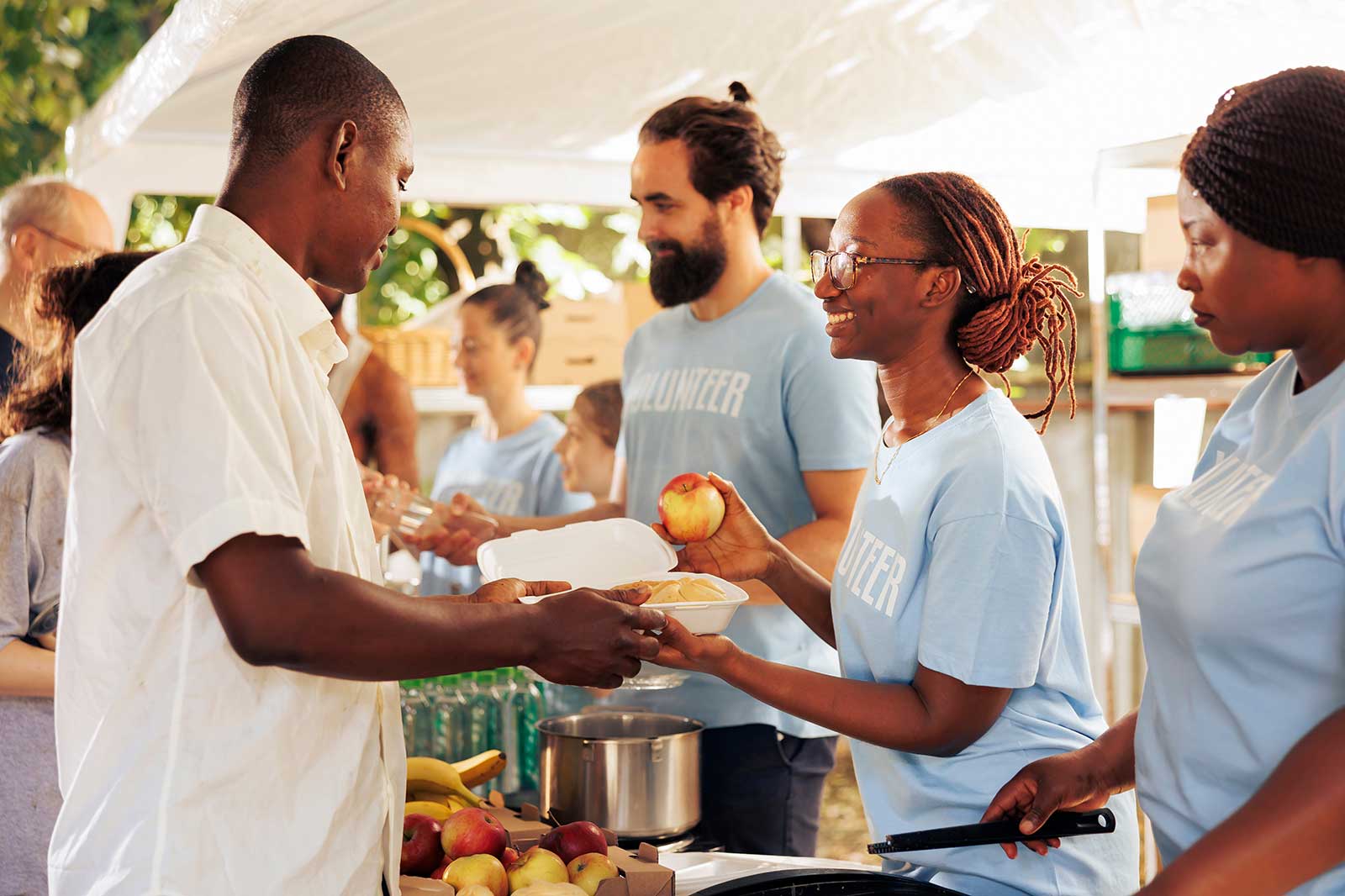 Volunteers distribute food at an outdoor event, handing out meals and fresh produce to those in need.
