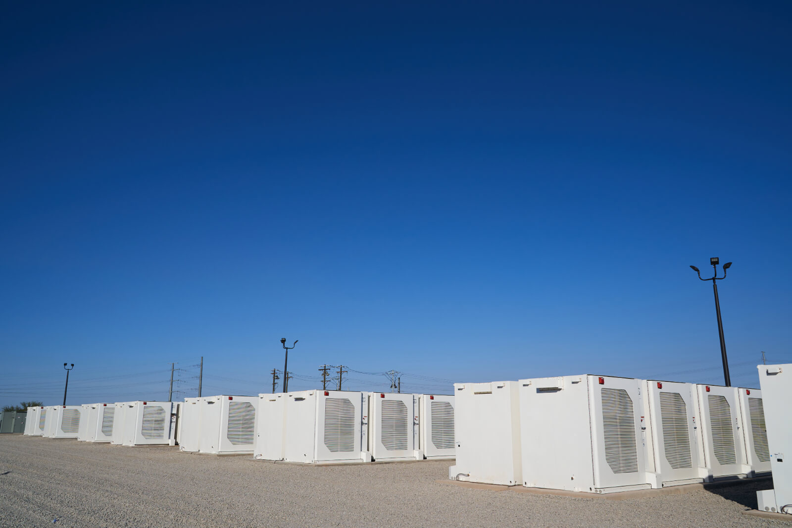A row of large white containers in an open area under a clear blue sky, with utility poles visible in the background.