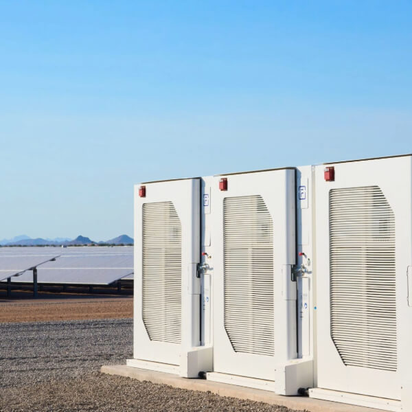 Three large white energy storage units stand in front of solar panels under a clear blue sky.