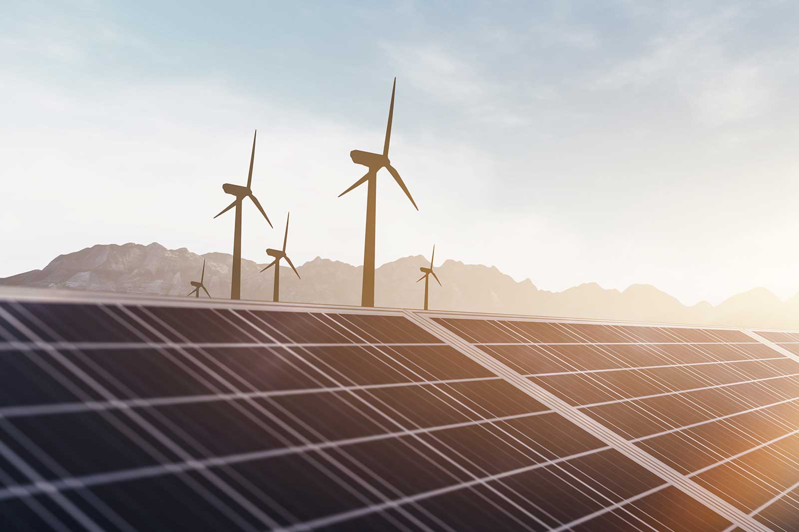 Solar panels in the foreground with wind turbines on a hillside under a bright sky, showcasing renewable energy sources.