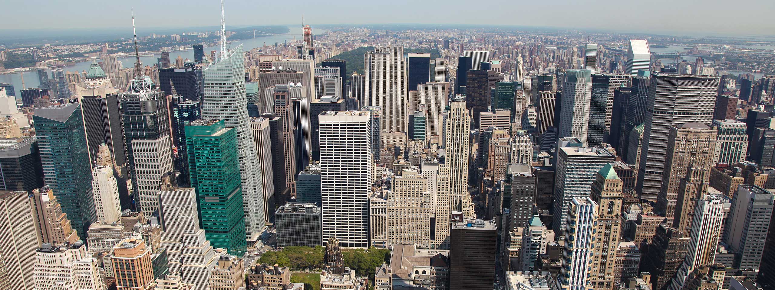 Aerial view of a bustling city skyline featuring tall skyscrapers and urban architecture under a clear blue sky.