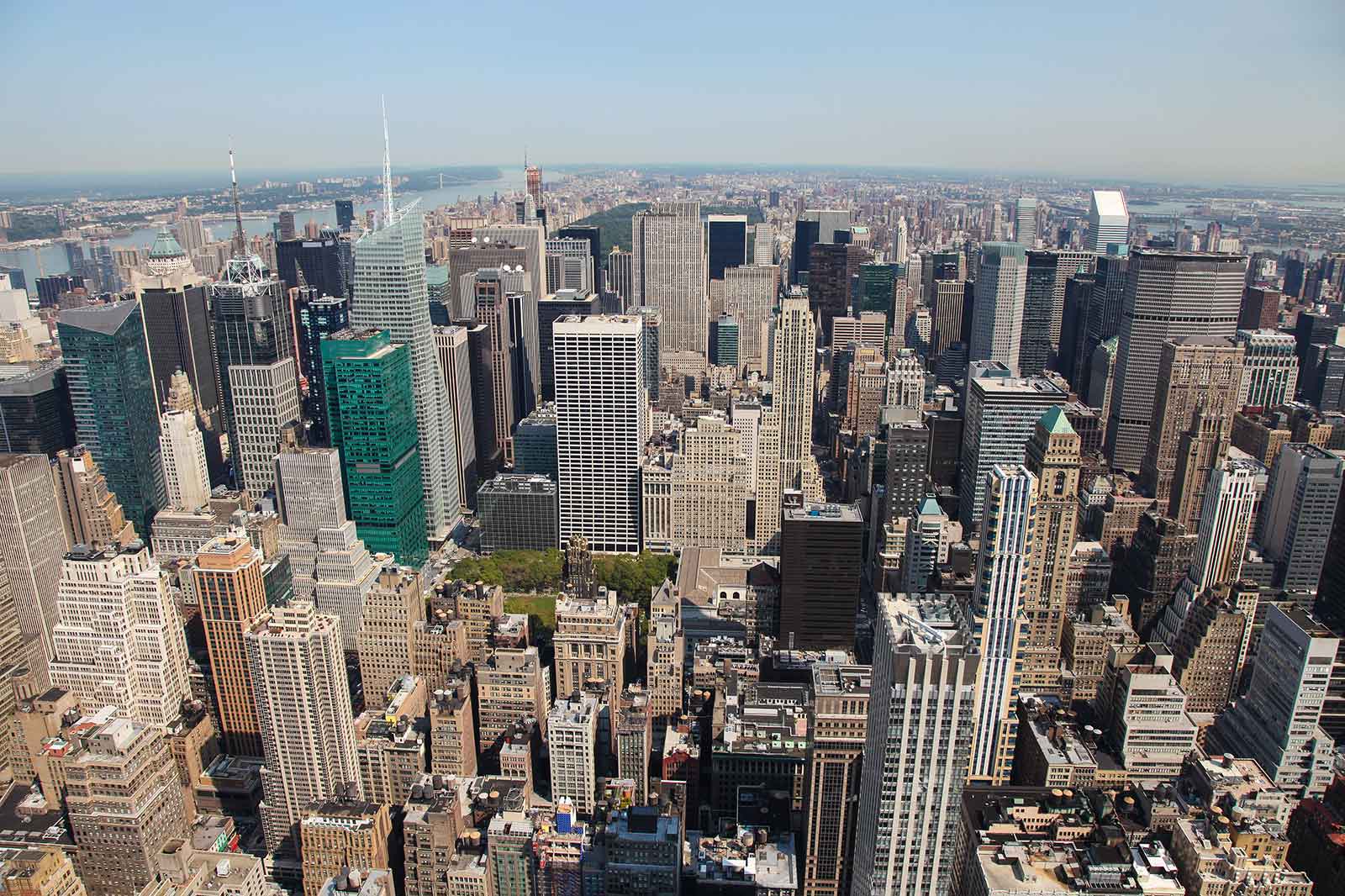Aerial view of New York City's skyline showcasing tall skyscrapers and green spaces under a clear blue sky.