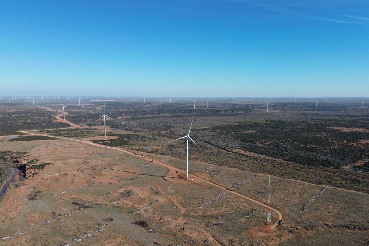 Aerial view of a wind farm in an open landscape with wind turbines and a clear blue sky.
